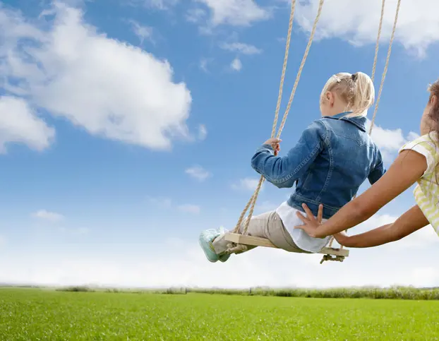 two children are swinging in the the grass field.